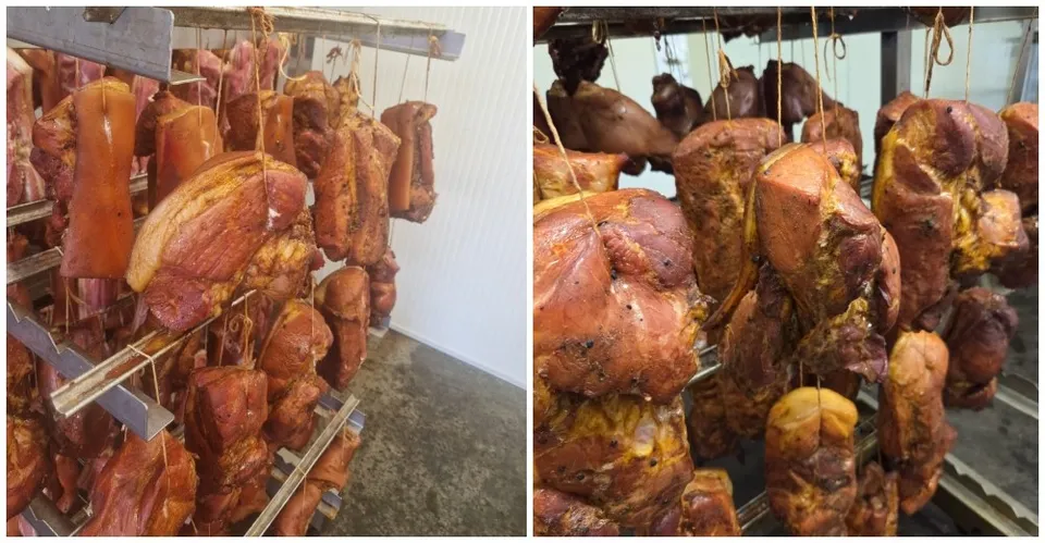 Diverse bucăți de carne afumată sunt suspendate de cârlige metalice într-un raft de depozitare.