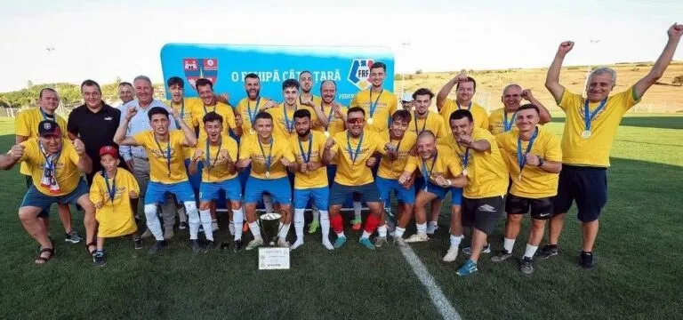 Un grup de bărbați îmbrăcați în tricouri galbene și pantaloni scurți stau pe un teren de fotbal cu brațele ridicate.
