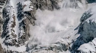 O masă mare de zăpadă și gheață se deplasează pe o versant abrupt de munte între stânci și formațiuni glaciare.