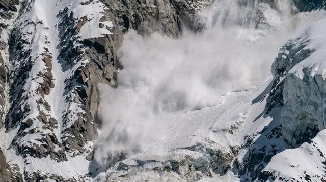 O masă mare de zăpadă și gheață se deplasează pe o versant abrupt de munte între stânci și formațiuni glaciare.
