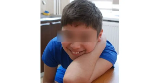Un copil cu părul scurt și tricou albastru stă sprijinit de o suprafață plană cu capul pe braț.