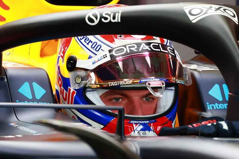 Un pilot de curse poartă un cască colorată cu logourile Oracle și Red Bull, fiind vizibil prin viziera deschisă în interiorul unui monopost de Formula 1.