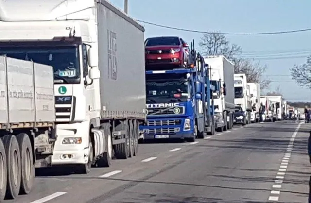 O coloană de camioane și autoutilitare circulă pe o autostradă sub un cer senin.