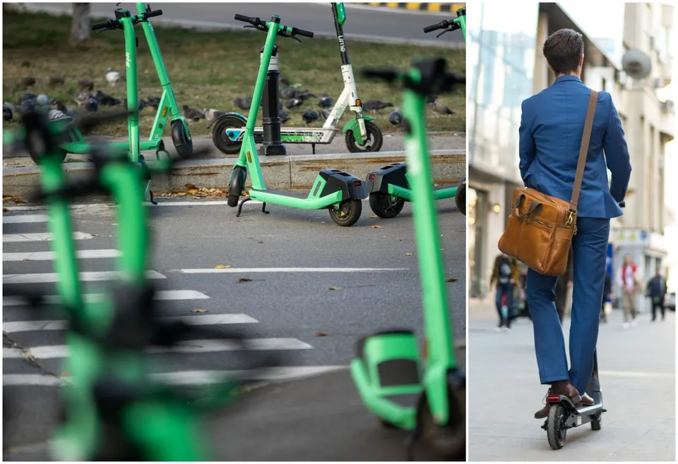 Un bărbat într-un costum albastru conduce o trotinetă electrică pe un trotuar, purtând o geantă de piele maro pe umăr.