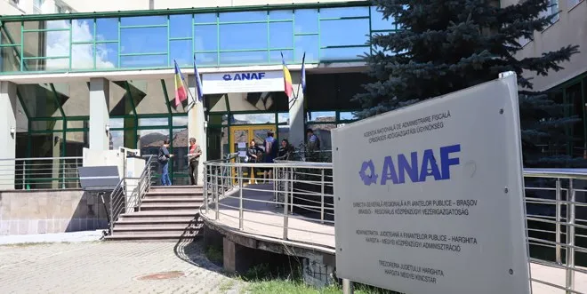 O clădire cu fațadă de sticlă prezintă o rampă de acces metalică, un panou informativ ANAF și câteva persoane lângă intrare.
