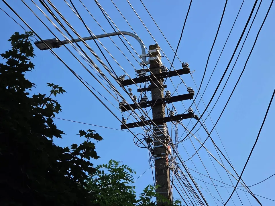 O stâlp de susținere a cablurilor electrice cu o mulțime de fire încălcate, dintr-un unghi coborât, pe fundalul unui cer albastru clar.