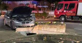 Un autoturism gri cu capota deschisă este oprit în fața unui cap de pod din beton pe marginea unui drum asfaltat noaptea.
