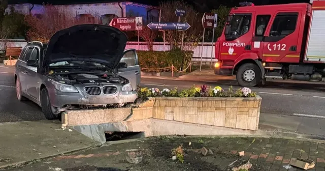 Un autoturism gri cu capota deschisă este oprit în fața unui cap de pod din beton pe marginea unui drum asfaltat noaptea.