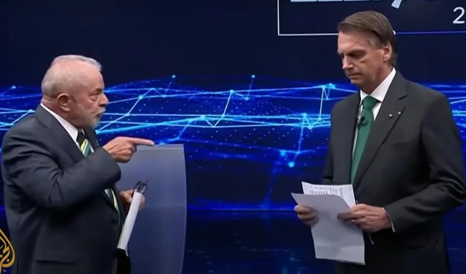 Doi bărbați în costum se află pe un fundal digital albastru cu grafice de rețea, unul arăând către celălalt while holding papers.