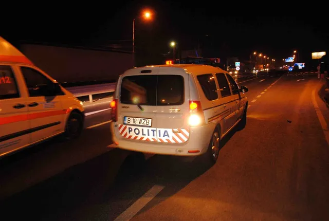 Un vehicul alb de poliție cu inscripție și număr de înmatriculare este parcat pe o stradă iluminată noaptea lângă o ambulanță.