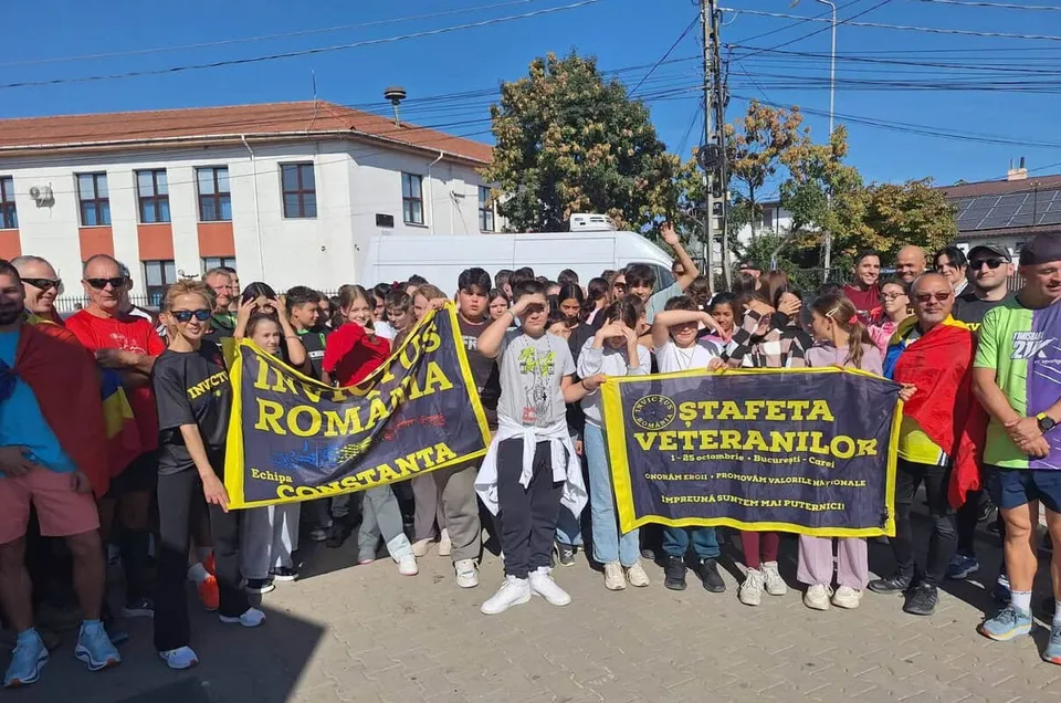 Un grup de oameni stă pe o stradă lângă două bannere colorate sub un cer senin.