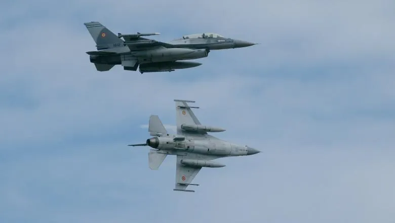 Două avioane de vânătoare gri zboară pe un cer înnegurat de nori.