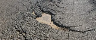 O apropiere a unui asfalt cracking cu un gropă mare expunând substratul nisipos sub suprafața deteriorată.