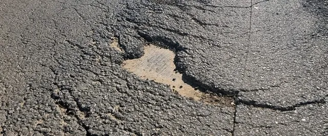 O apropiere a unui asfalt cracking cu un gropă mare expunând substratul nisipos sub suprafața deteriorată.