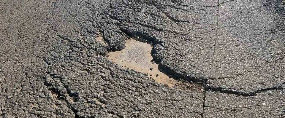 O apropiere a unui asfalt cracking cu un gropă mare expunând substratul nisipos sub suprafața deteriorată.