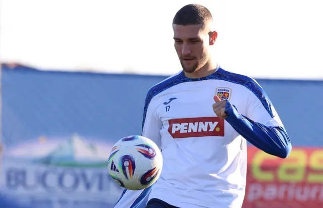 Un bărbat cu tricou alb și mâneci albastre poartă un echipament sportiv și privește un fotbal aflat în aer în fața lui.