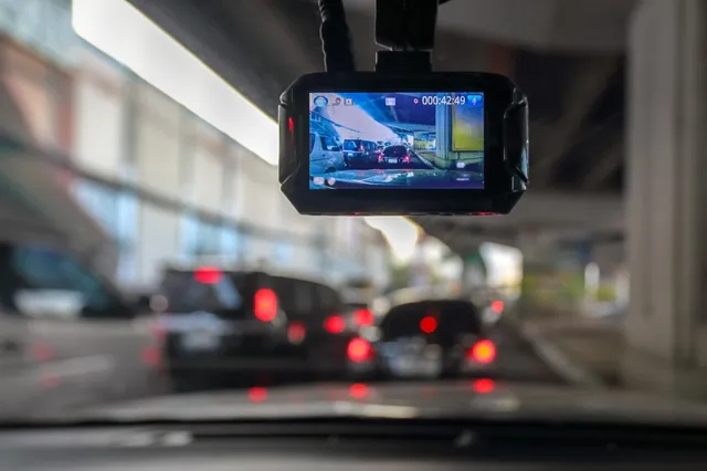 O cameră de bord suspendată afișează o filmare a unor mașini pe un drum, în timp ce traficul din fundal este neclar și desfășurat.