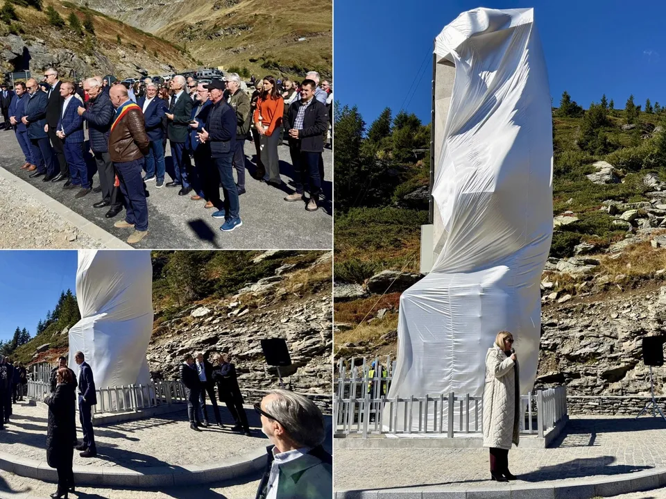 Un monument înalt este acoperit de un material alb, fiind înconjurat de un grup de persoane pe un teren pietos sub un cer senin.