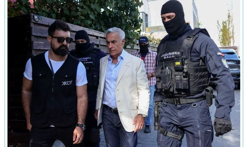 Un bărbat cu sacou deschis merge pe stradă înconjurat de un bărbat cu vestă neagră și de doi agenți în uniformă de poliție și măști negre.