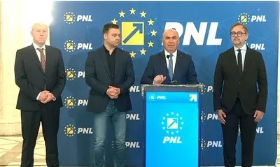 Patru bărbați în costume și haine casual stau în picioare în fața unui panou albastru cu logoul PNL.