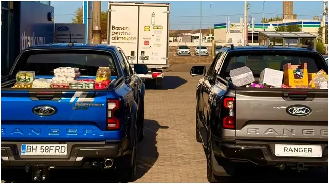 Două pickup-uri parcate pe o suprafață pavată transportă cutii și pachete de alimente în benzi de încărcare deschise.