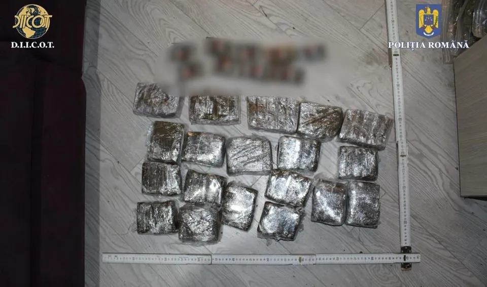 Mai multe pachete dreptunghiulare învelite în folie de aluminiu sunt așezate pe un podea de lemn lângă o riglă de măsurare albă.