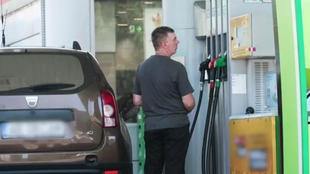 Un bărbat stă lângă o pompă de benzină lângă partea din spate a unei mașini maronii.