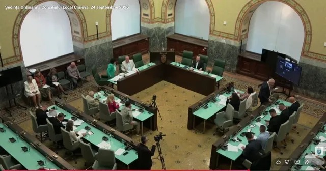 Oamenii stau la mese lungi cu suprafețe verzi într-o sală cu pereți înalți și ferestre arcuite, încadrați de un birou central în formă de L.