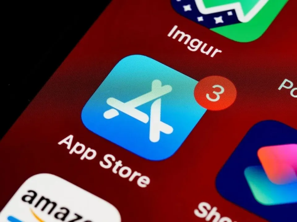 Un ecran de smartphone afișează iconița App Store pe un fundal roșu, având un indicator de notificare roșu cu cifra trei.