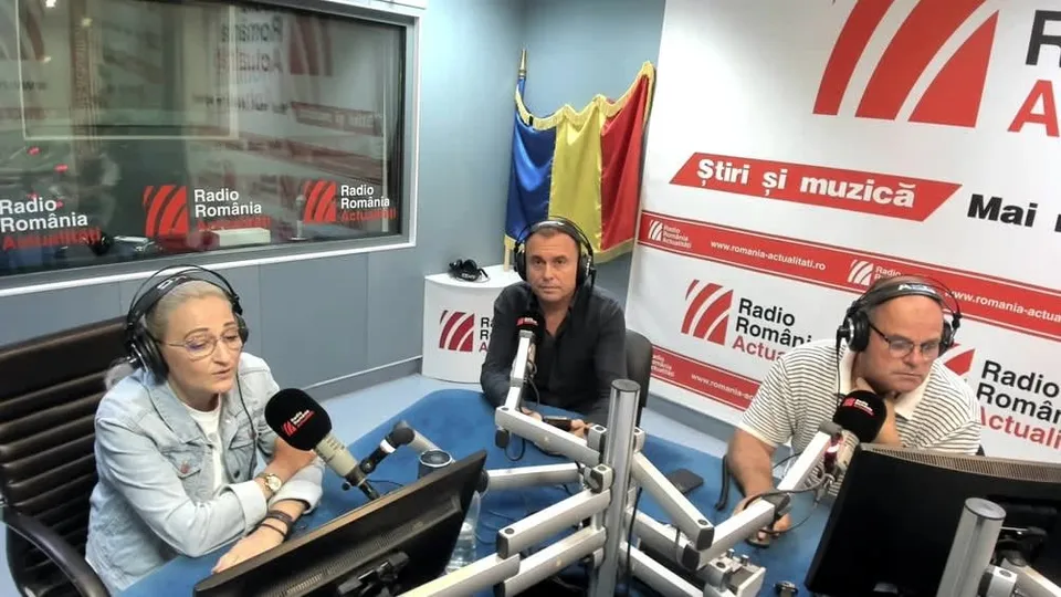 Trei persoane cu căști de ascultare stau la mese cu microfoane într-un studio de radio.