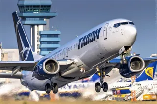 Un avion de pasageri gri cu inscripția TAROM decolă de pe o pistă, având două motoare suspendate sub aripi și trenul de aterizare extins.