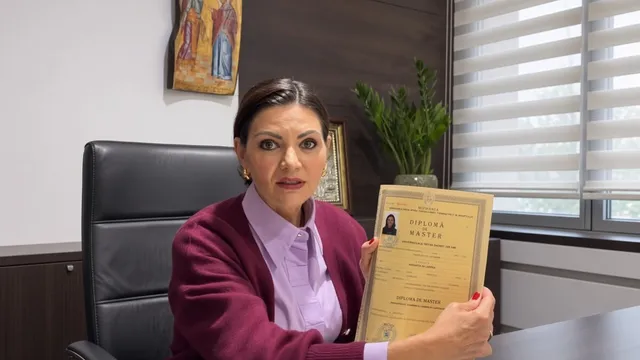 O femeie cu părul închis la culoare, purtând o sacou purpuriu și o cămașă lila, ține în mâini o diplomă de master într-un dosar galben.