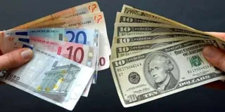 Două mâini țin grupuri de bancnote de euro și dolari întinse pe un fundal închis.