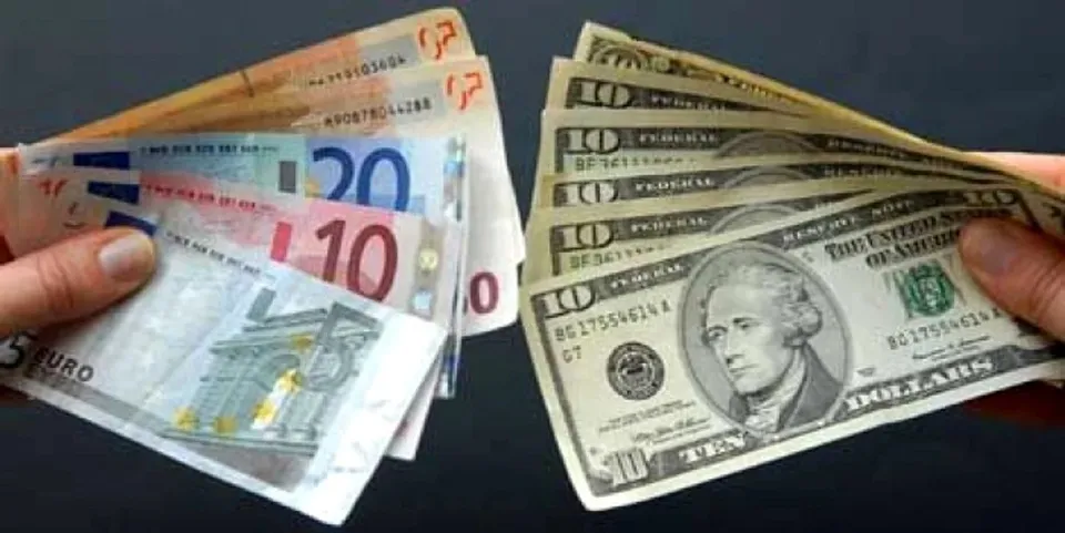 Două mâini țin grupuri de bancnote de euro și dolari întinse pe un fundal închis.
