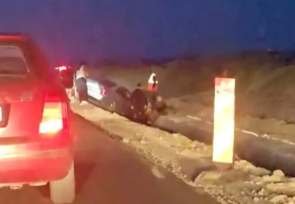 Un autoturism gri este poziționat într-un șanț de lângă un drum, lângă un vehicul roșu și un stâlp de semnalizare vertical.