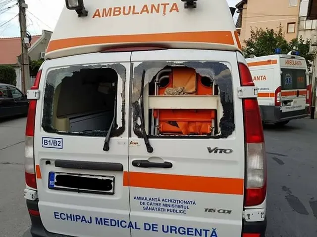 Spatele unei ambulanțe albe cu ferestre sparte dezvăluie un echipament medical portocaliu în interiorul vehiculului.