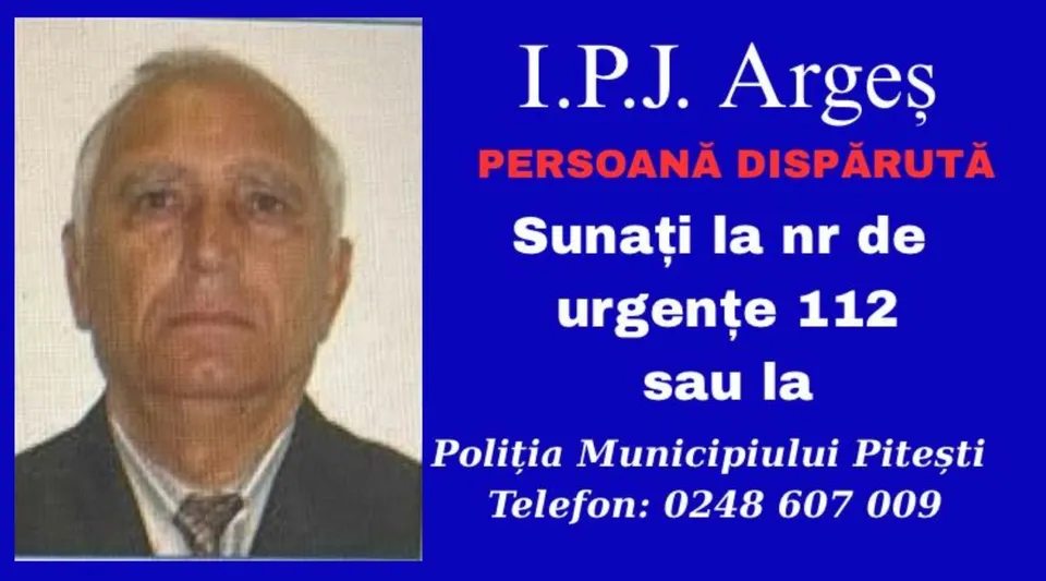 Un bărbat în vârstă, cu părul scurt și gri, poartă o jachetă închisă la culoare peste o cămașă și o cravată, pe un fundal albastru cu text.