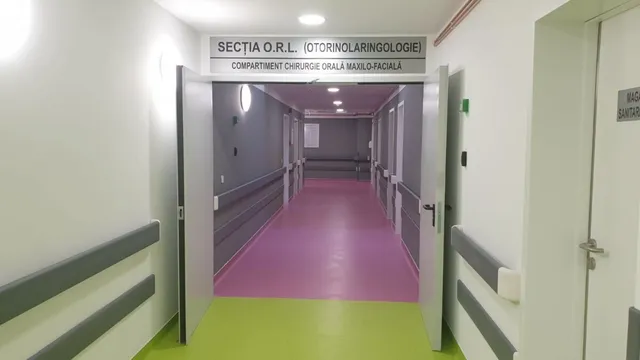 Un hol de spital cu pereți albi, pardoseală mov și verde, și un panou deasupra unei intrări care indică secția O.R.L.