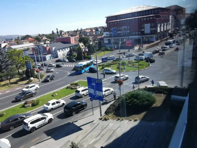 O vedere de sus a unei intersecții stradale cu mai multe mașini, un autobuz albastru și clădiri în fundal sub un cer senin.