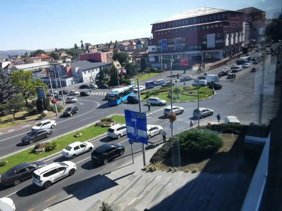 O vedere de sus a unei intersecții stradale cu mai multe mașini, un autobuz albastru și clădiri în fundal sub un cer senin.