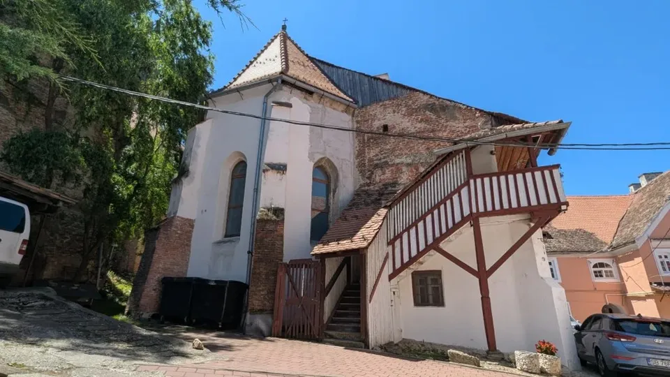 O clădire albă cu acoperiș de țiglă, un pridvor din lemn și un perete de cărămidă expusă sub un cer senin.