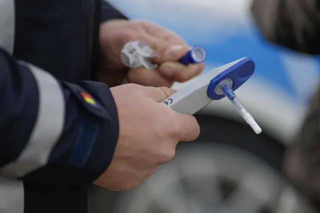 O persoană ține un dispozitiv alb cu un tub de testare atașat și un obiect mic, transparent, în mâini.
