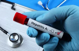 O mână îmbrăcată în mănușă albastră ține un recipient de probă de sânge cu eticheta Hepatitis A pe un fundal cu stetoscoap și documente medicale.