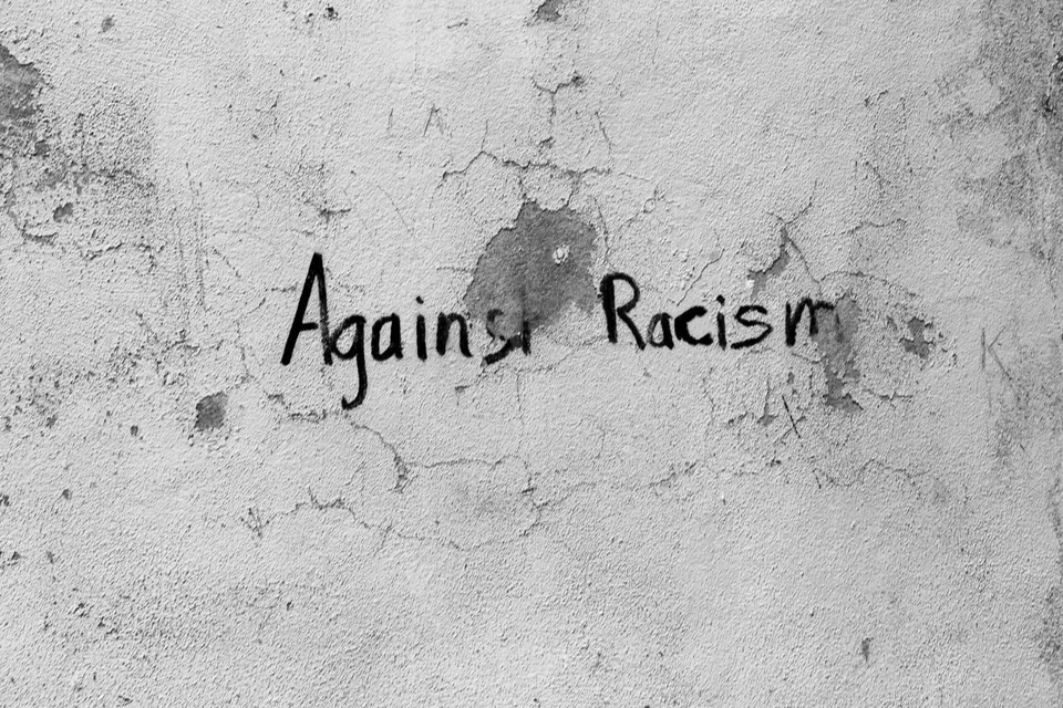 Textul scris cu negru pe un perete gri și crăpat spune Against Racism.
