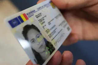 O persoană ține un document de identitate românesc care prezintă o fotografie de tip portret și diverse informații scrise pe un fundal albastru.