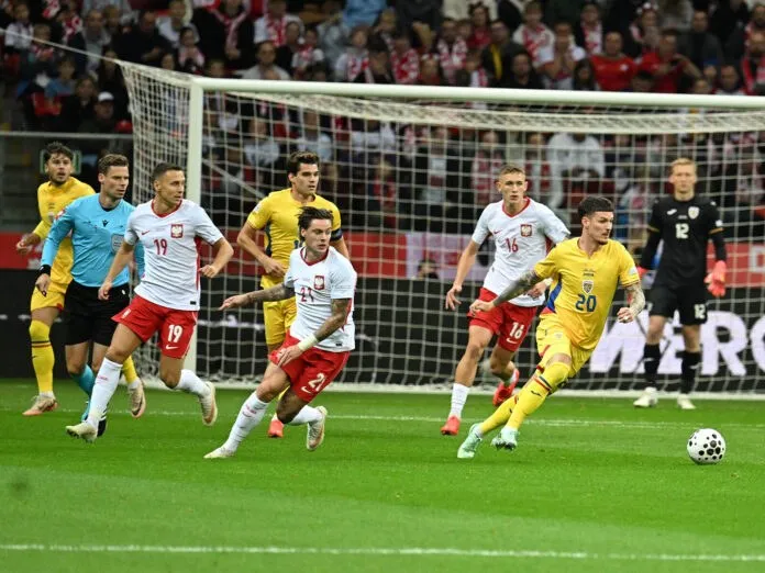 Câțiva jucători de fotbal în echipamente albe și galbene aleargă pe un teren verde lângă un gol, în timp ce un fotbal se află pe iarbă.