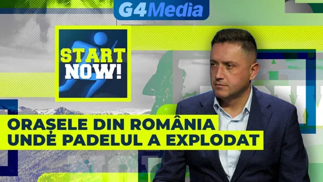Un bărbat cu sacou și cămașă deschisă stă în fața unui fundal colorat cu text și grafice.