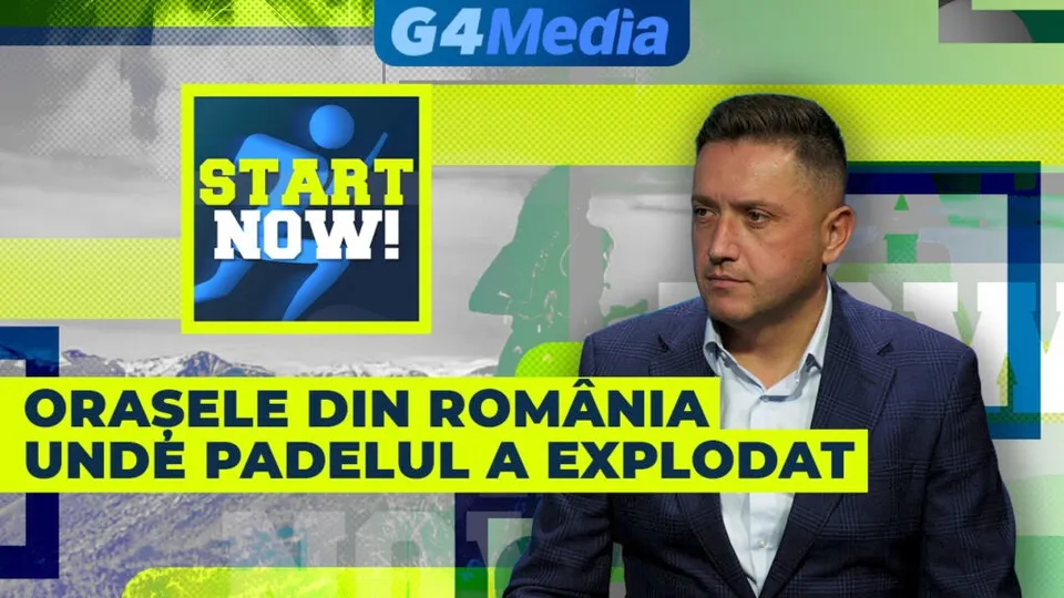 Un bărbat cu sacou și cămașă deschisă stă în fața unui fundal colorat cu text și grafice.