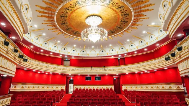 Interiorul unui auditorium cu scaune roșii, pereți roșii și un candelabru mare suspendat sub o cupolă decorată cu motive aurii.