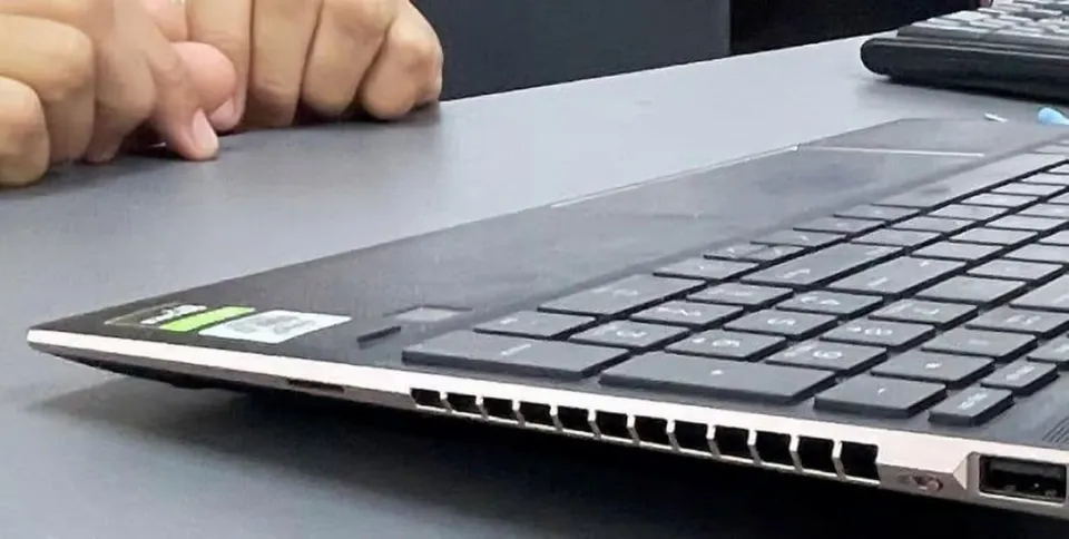 O persoană stă cu mâinile încleștate pe o masă lângă un laptop deschis.